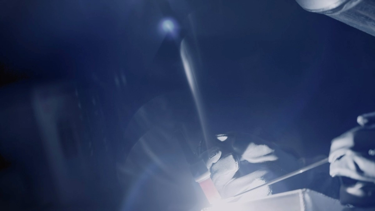 Close view of gloved hands guiding a welding torch and filler rod at a bright weld.